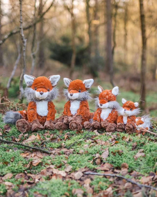 4 Fuchs Kuscheltiere von Wrendale Designs und ein Fuchs Schlüsselanhänger. Die Füchse sitzen in einer Reihe im Wald und sind nach der Größe geordnet.