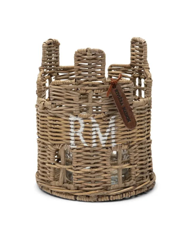 In Handarbeit gefertigtes Windlicht aus Rattan im Stil eines runden Hauses. Auf dem hellbraunen Ratten ist das Kürzel "RM" in weiß aufgemalt. Das Windlicht hat drei "Seiten", wobei sich auf jeder Seite drei Fenster und ein Schornstein befinden. Das mitgelieferte Glas findet im Inneren des Hauses Platz. Ein ledernes Riviera Maison Schildchen ist ebenfalls am House Votive angeknotet.