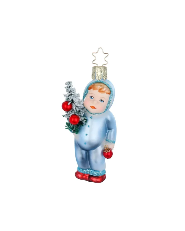 Schneekind Weihnachtsbaumschmuck von Inge Glas handgefertigt in Deutschland. Das süße Schneekind trägt rote Schühchen, einen hellblauen Schneeanzug und in den Händen einen kleinen Tannenbau mit roten Weihnachtsbaumkugeln und eine einzelne Kugel in der anderen Hand. Kapuze und Säume des Schneeanzugs sind mit blauen Glitzer Highlights versehen.