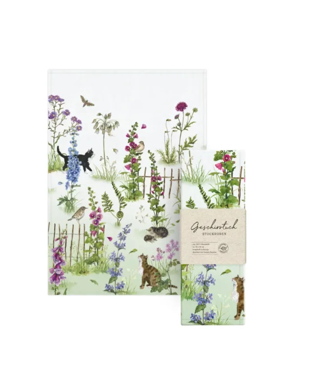 Geschirrtuch Stockrosen vom Grätz Verlag zusammen mit der Verpackung. Sommerliches Motiv von Daniela Drescher mit Blüten, Tieren und Gartenzaun.